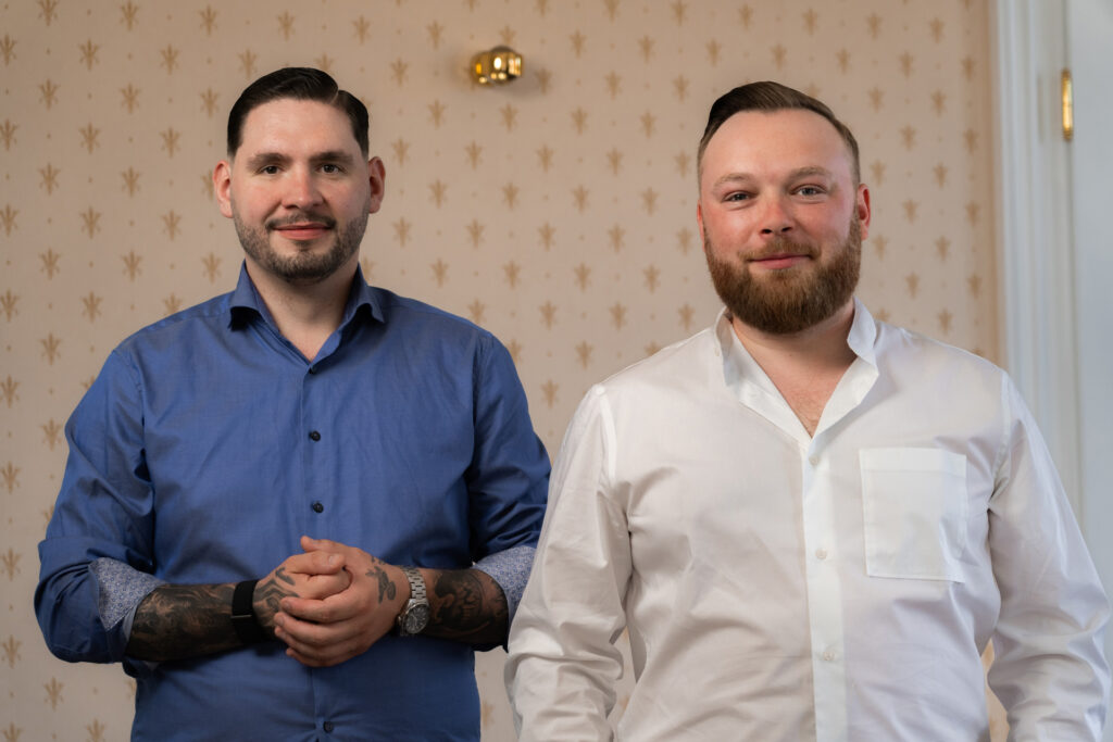 Ein portrait von zwei Jungen Männern. Sie sind schick angezogen und lächeln